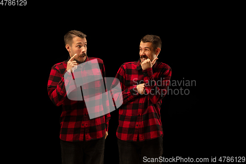 Image of Young handsome man arguing with himself on black studio background.