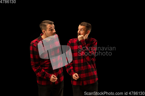 Image of Young handsome man arguing with himself on black studio background.