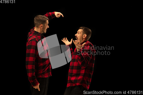 Image of Young handsome man arguing with himself on black studio background.