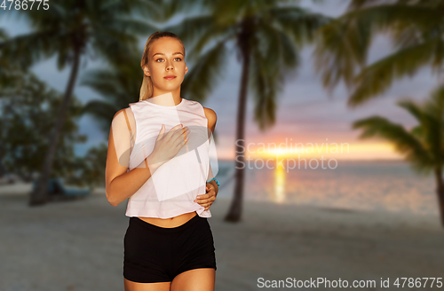 Image of happy young woman running along tropical beach