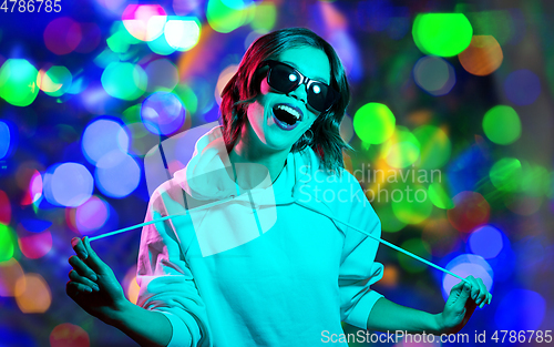 Image of woman in hoodie and sunglasses over night lights