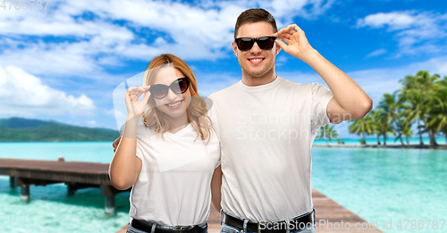 Image of happy couple in t-shirts and sunglasses on beach