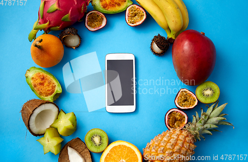Image of exotic fruits around smartphone on blue background