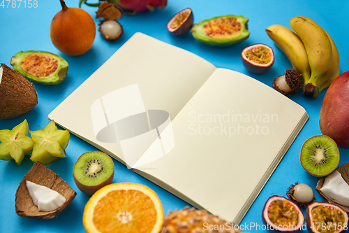 Image of exotic fruits around notebook with empty pages