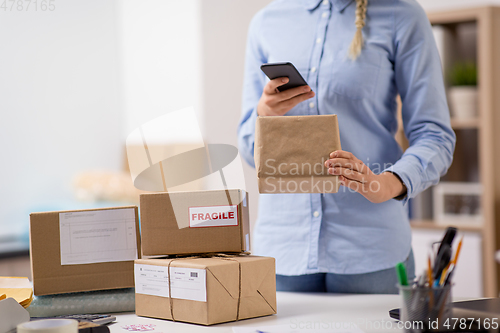 Image of woman with smartphone and parcels at post office