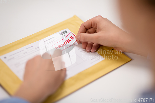 Image of hands sticking fragile marks to parcel in envelope