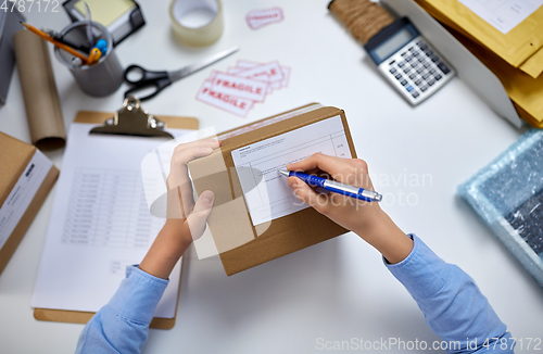 Image of close up of hands filling form on parcel at office