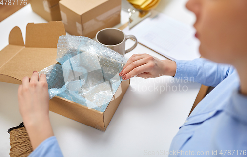 Image of woman packing mug to parcel box at post office