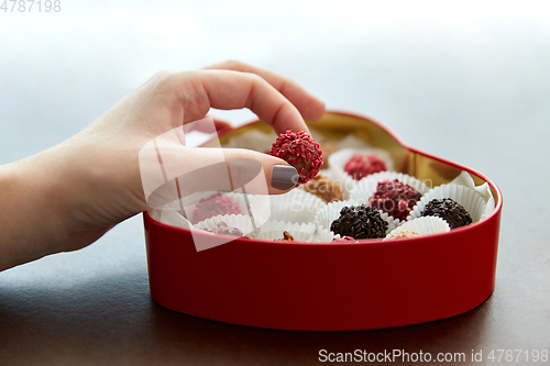 Image of hand with candies in heart shaped chocolate box