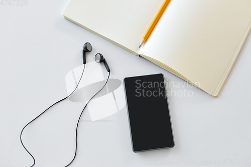 Image of earphones, smartphone and notebook with pencil