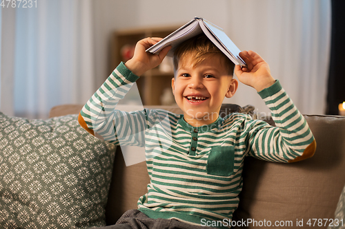 Image of happy little boy with book having fun at home