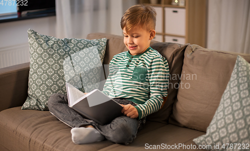 Image of happy smiling little boy reading book at home