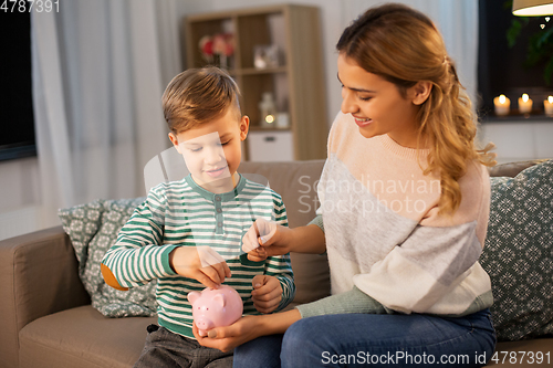 Image of mother and little son with piggy bank at home