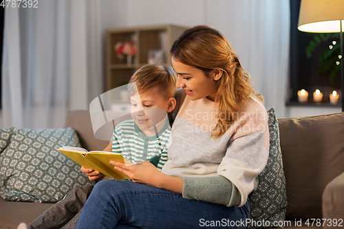 Image of happy mother and son reading book sofa at home