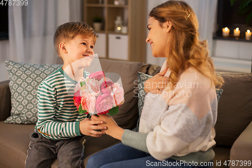 Image of smiling little son gives flowers to mother at home