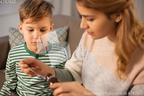 Image of mother giving medication or cough syrup to ill son