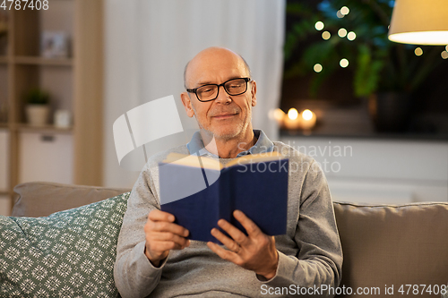 Image of happy bald senior man on sofa reading book at home