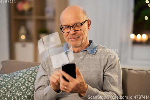 Image of happy senior man texting on smartphone at home