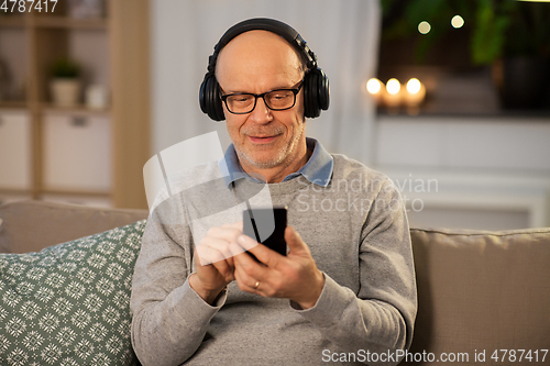 Image of senior man with smartphone and headphones at home