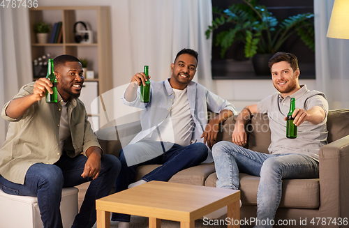 Image of happy male friends drinking beer at home at night