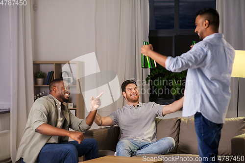 Image of happy male friends drinking beer at home at night