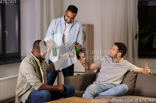 Image of happy male friends drinking beer at home at night