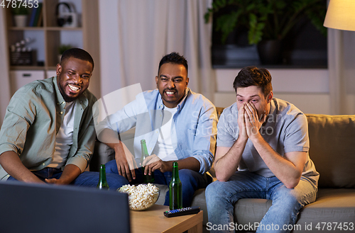 Image of happy male friends with beer watching tv at home