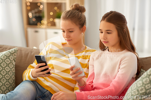 Image of girls with smartphones sitting on sofa at home