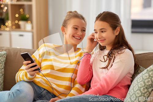 Image of happy girls with smartphone and earphones at home