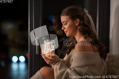 Image of woman with garland lights in glass mug at home