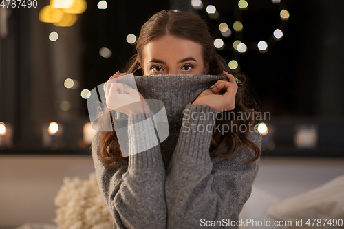 Image of young woman in woolen sweater at home at night