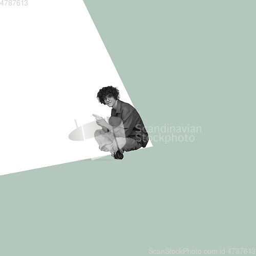 Image of Modern design, contemporary art collage. Inspiration, idea, trendy urban magazine style. Young man sitting in white angle on pastel green background