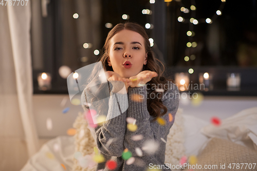 Image of woman blowing confetti from her hands at home