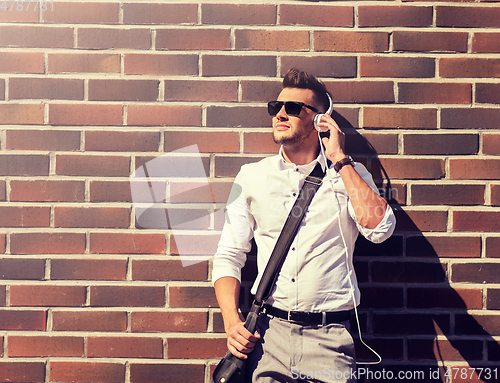 Image of young man in headphones with bag over brickwall