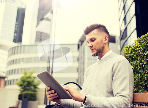 Image of man with tablet pc sitting on city street bench