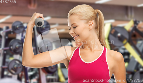 Image of happy young woman with dumbbells exercising in gym