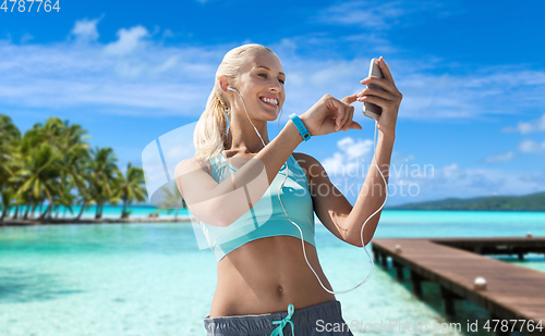 Image of happy woman with smartphone and earphones on beach