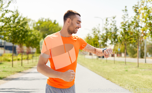 Image of smiling man with smart watch running outdoors