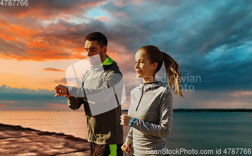 Image of couple with fitness trackers running over sea