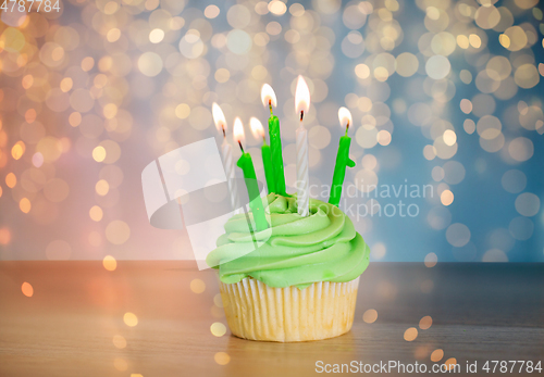 Image of green cupcake with six burning candles on table