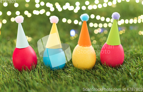 Image of easter eggs in party hats on artificial grass