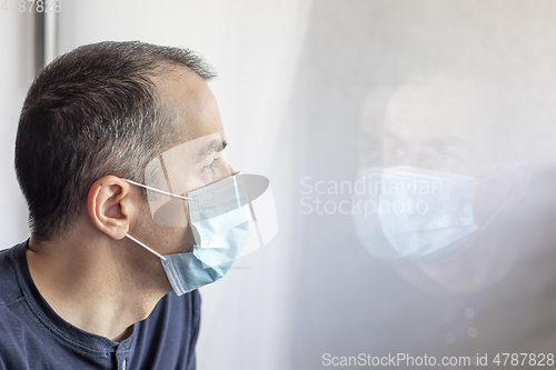 Image of Young man with medical mask looking out the window