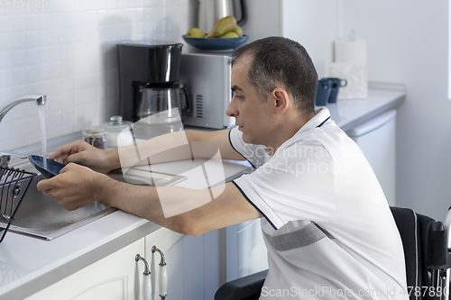 Image of Young Happy Disabled Man On Wheelchair Washing Dishes