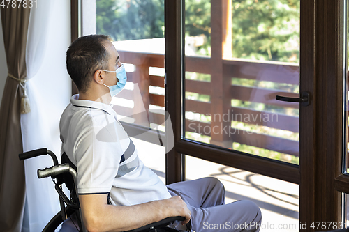 Image of young man wearing face mask sitting in a wheelchair alone lookin