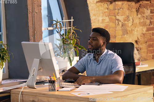 Image of African businessman, manager working in modern office using devices and gadgets