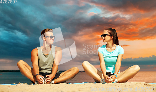 Image of smiling couple stretching legs on beach