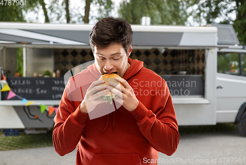 Image of hungry young man eating hamburger at food truck