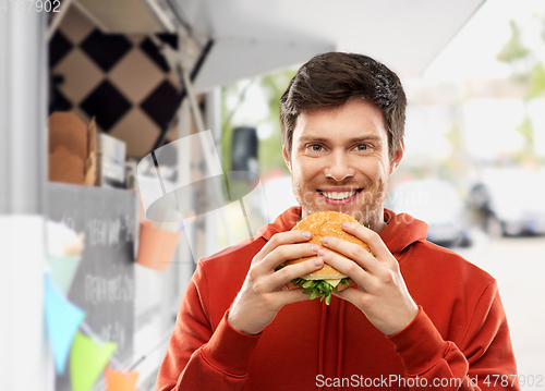 Image of happy young man eating hamburger at food truck