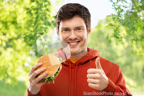 Image of happy young man with hamburger showing thumbs up