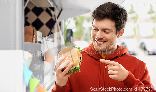 Image of happy young man showing hamburger at food truck